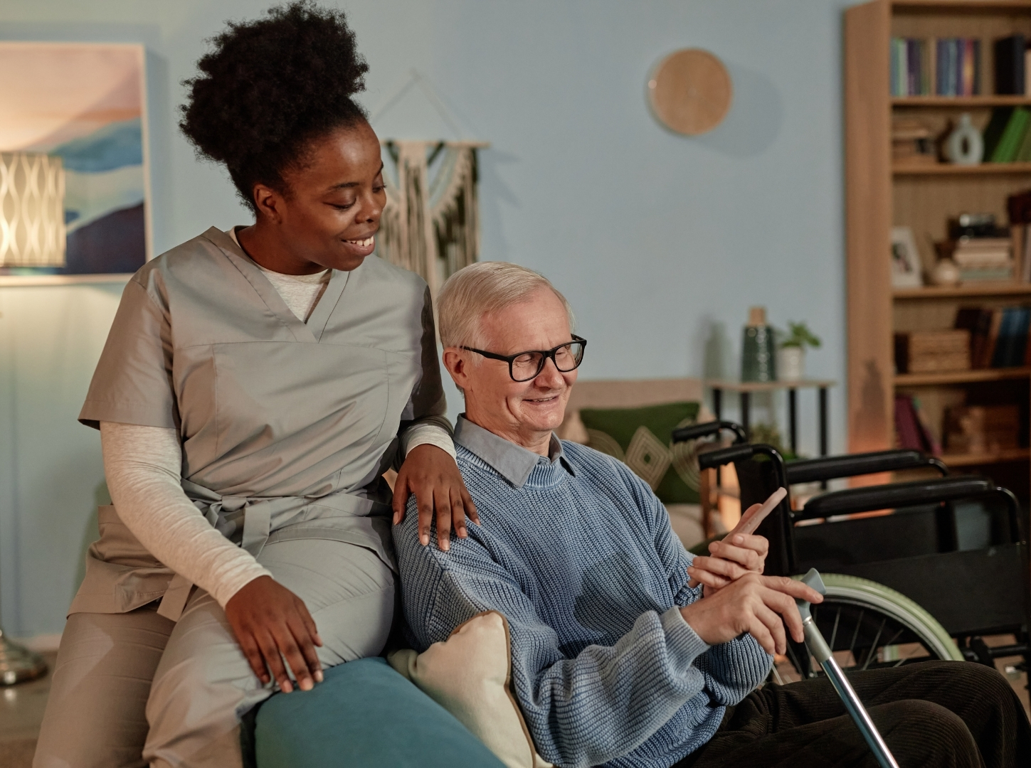 Black Female Caregiver Assisting Elderly Man Providing Help with Phone at Home